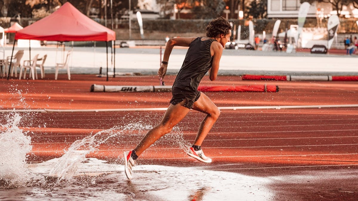Dynamic shot of an athlete sprinting on a wet track, capturing motion and energy.